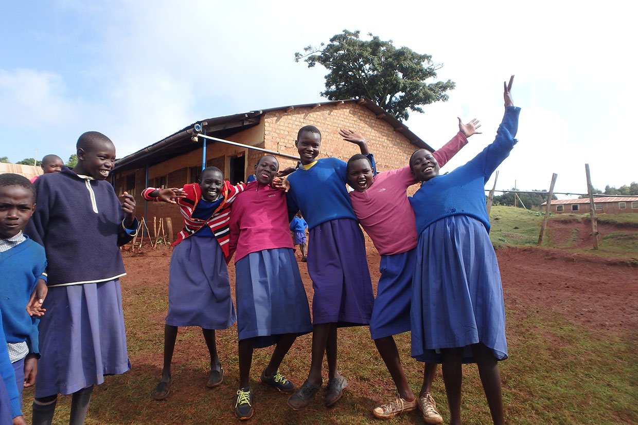 Group of school children in uniforms smiling and playing outdoors in front of a brick building.