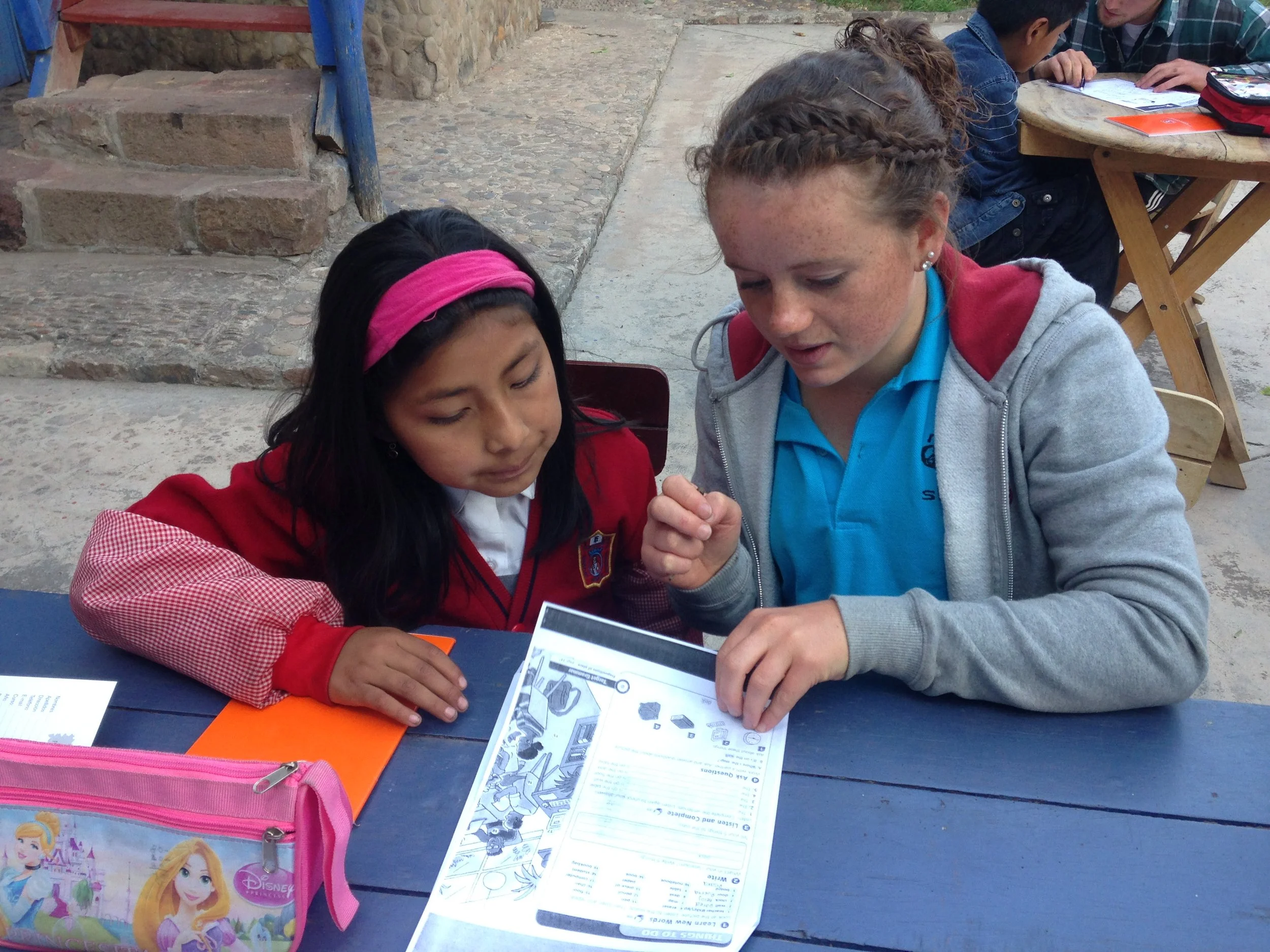 Scenic view of mountains, a lake, and rolling hills with grass and shrubbery in the foreground under a cloudy sky.