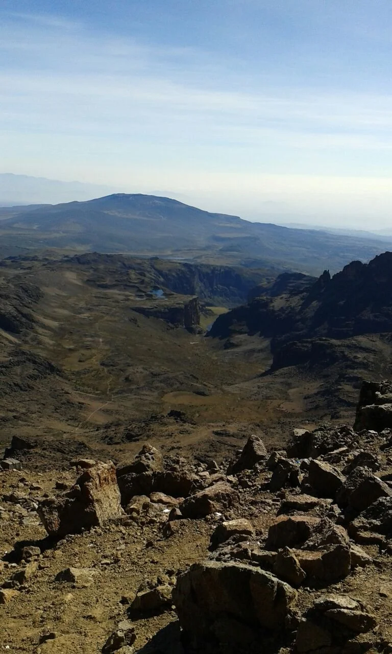 A vast, rocky mountainous landscape with a view of distant mountains under a partly cloudy sky.