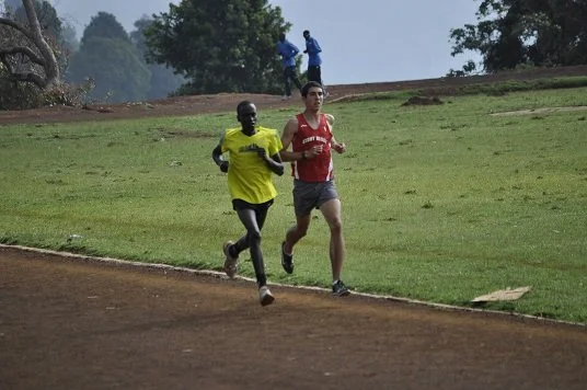 Two men running on a track, one in a yellow shirt and the other in a red shirt.