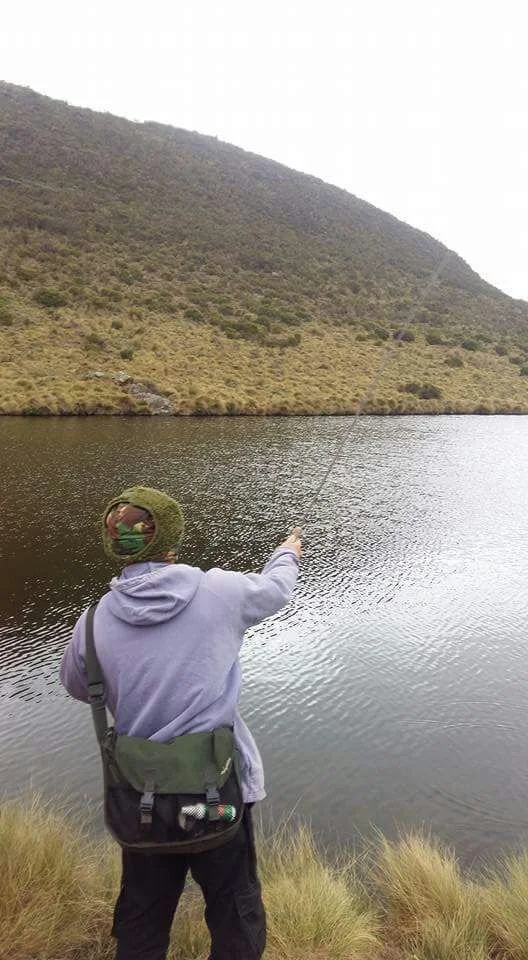 Person fishing by a lake with a hillside in the background.