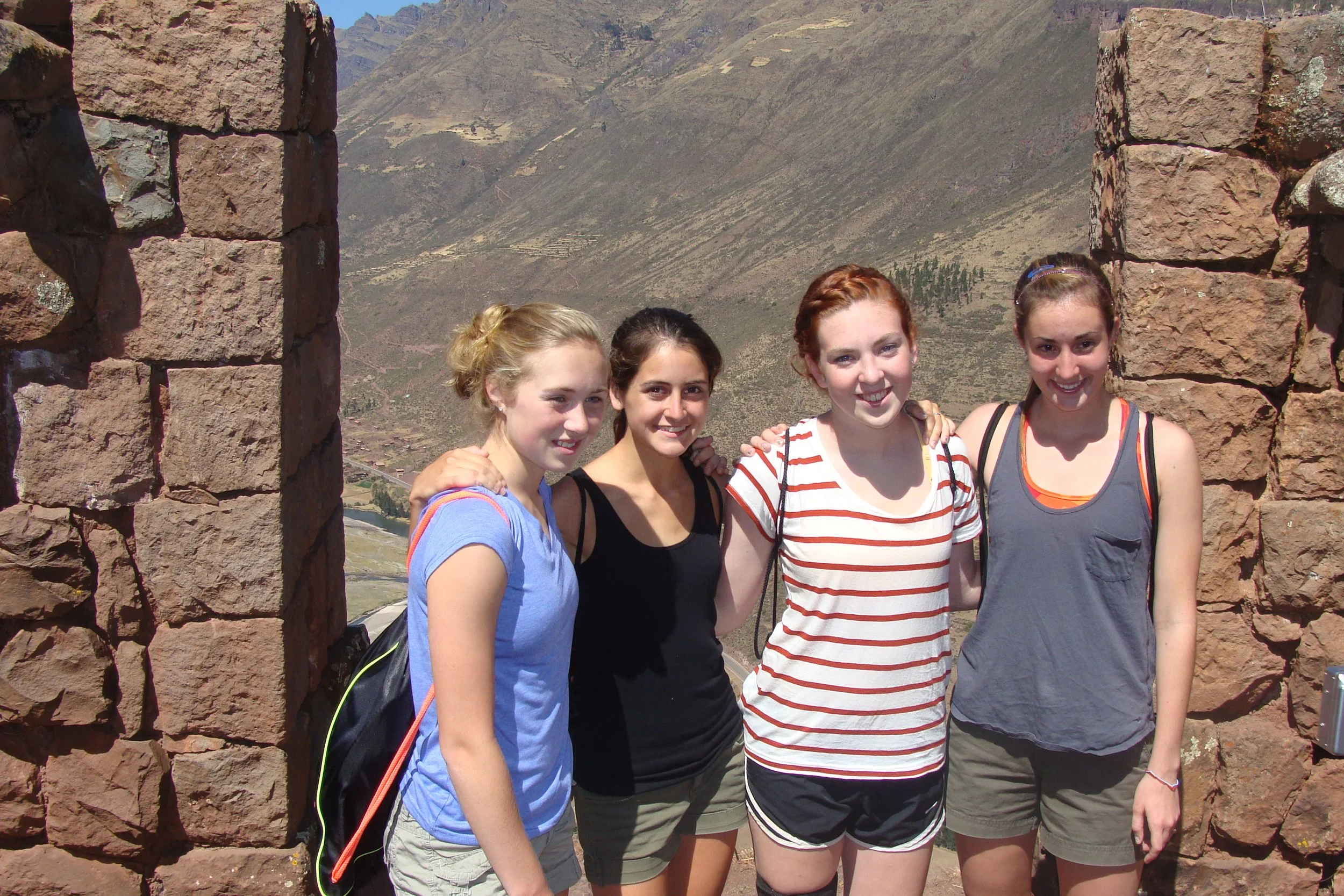 Four young women standing together on a mountain overlook with desert landscape in the background.