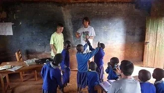 Children and a teacher in a classroom, with children raising their hands.