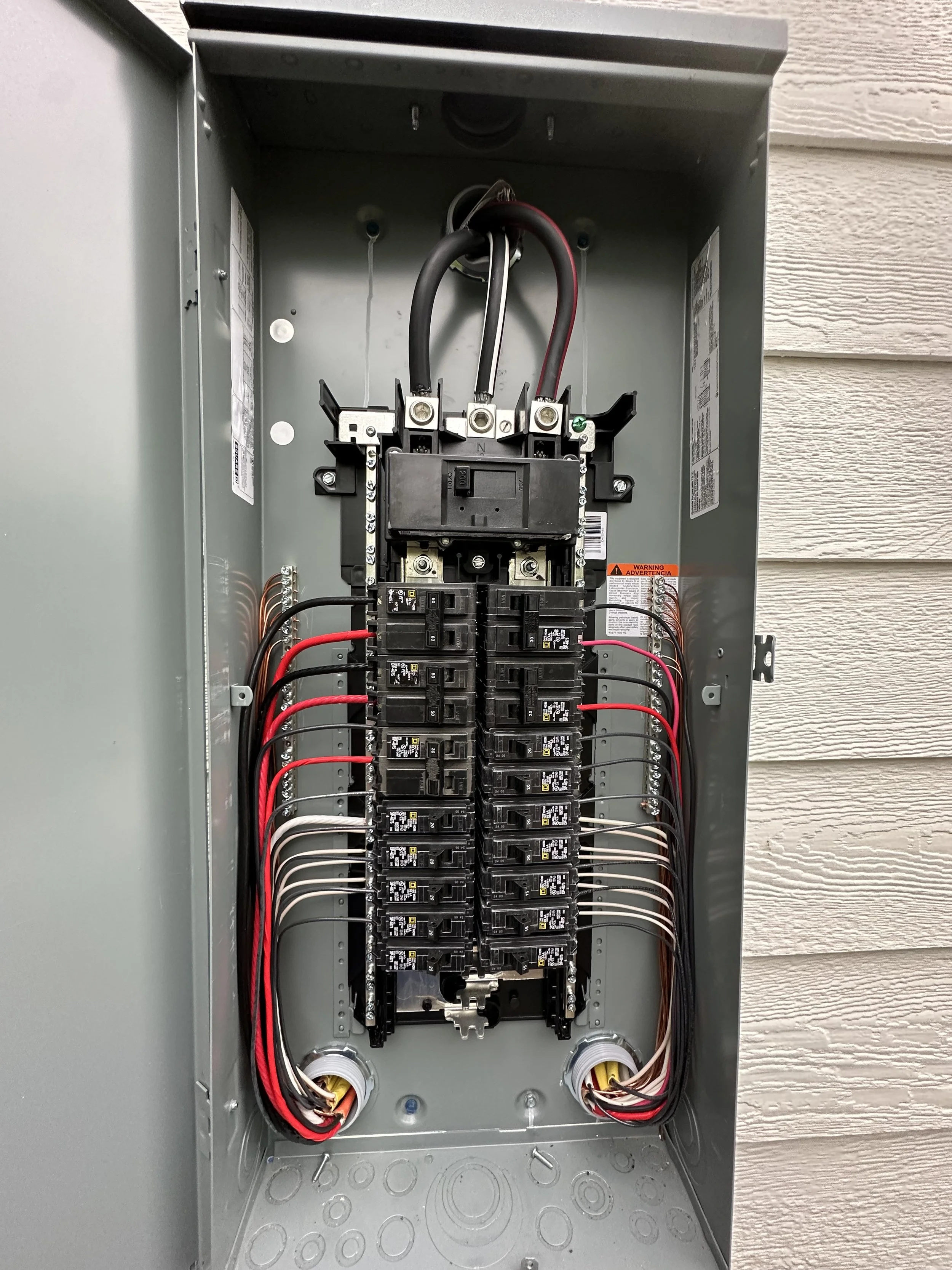Open electrical panel box with multiple circuit breakers and wiring.