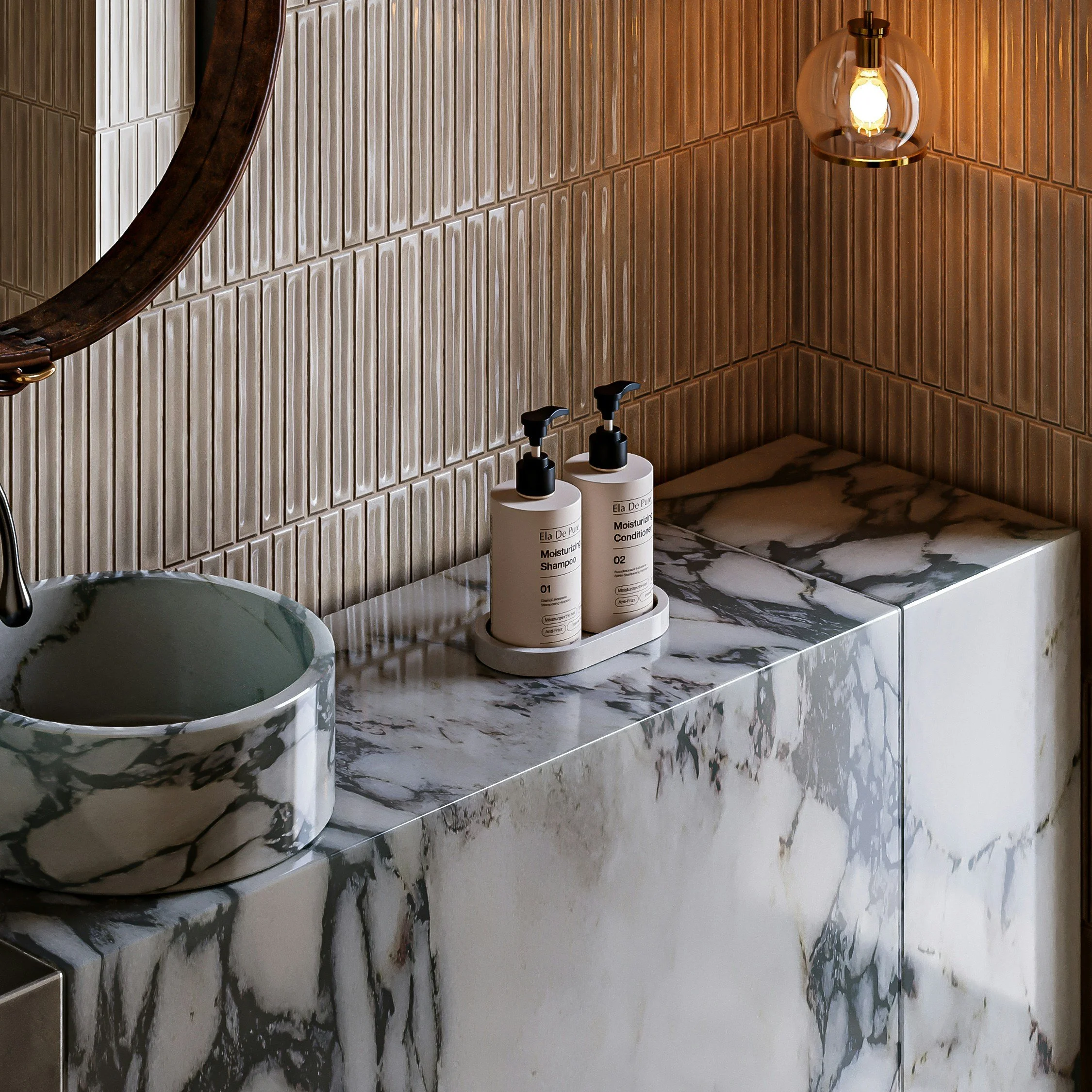 Bathroom sink area with marble countertop, round marble sink, two pump bottles of moisturizer and shampoo, brown tiled walls, and a hanging light fixture.
