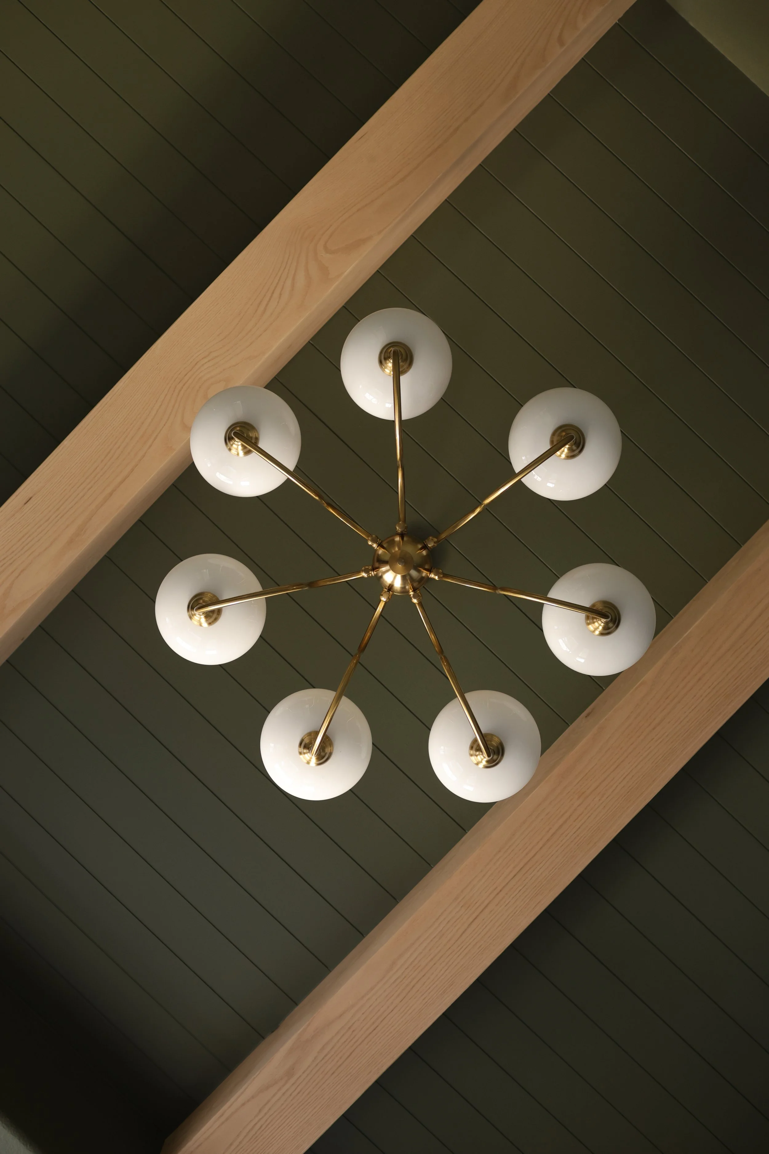Ceiling light fixture with eight white globe bulbs attached to brass rods, hanging from a brass center, against a dark ceiling with wooden beams.