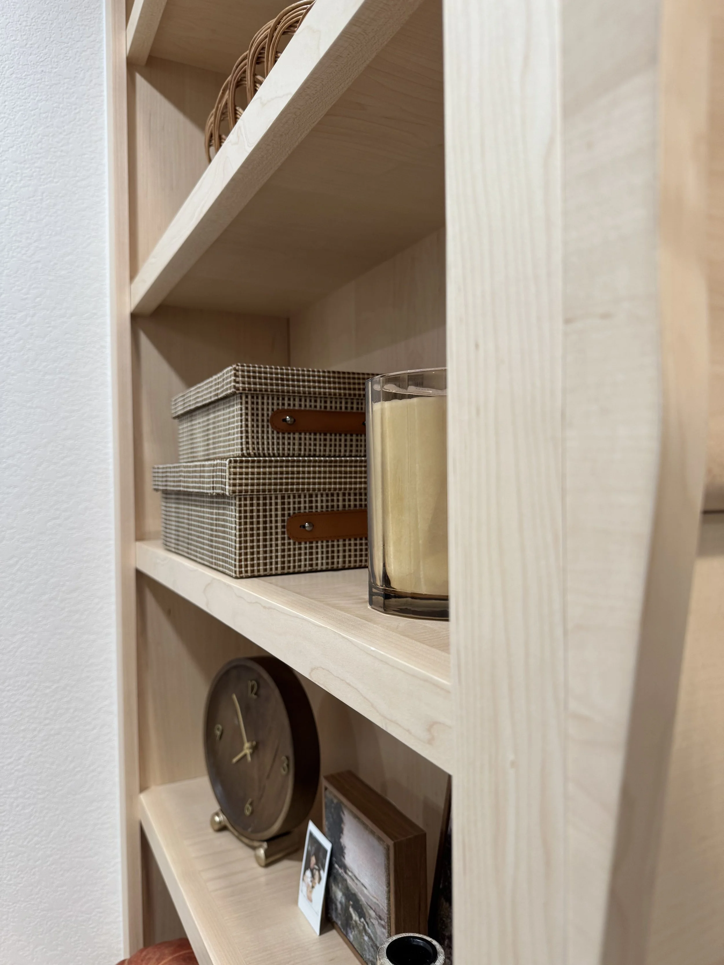 Wooden bookshelf with two patterned storage boxes, a candle, a clock, small framed photos, and decorative items