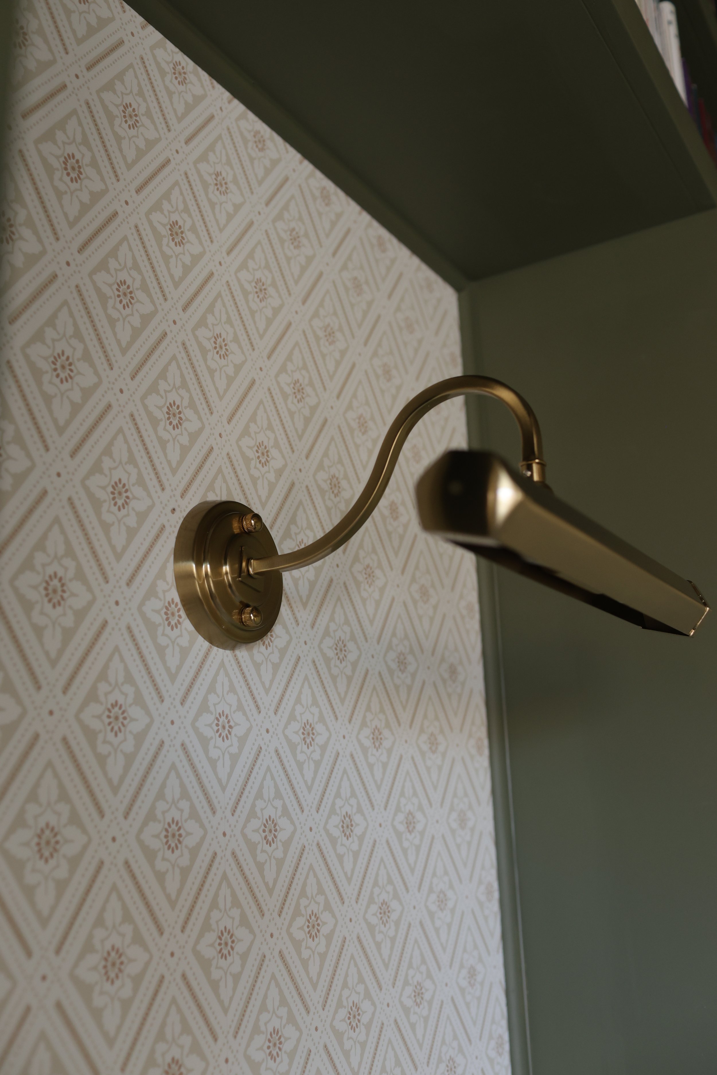 Close-up of a silver wall-mounted light fixture in a room with patterned wallpaper.