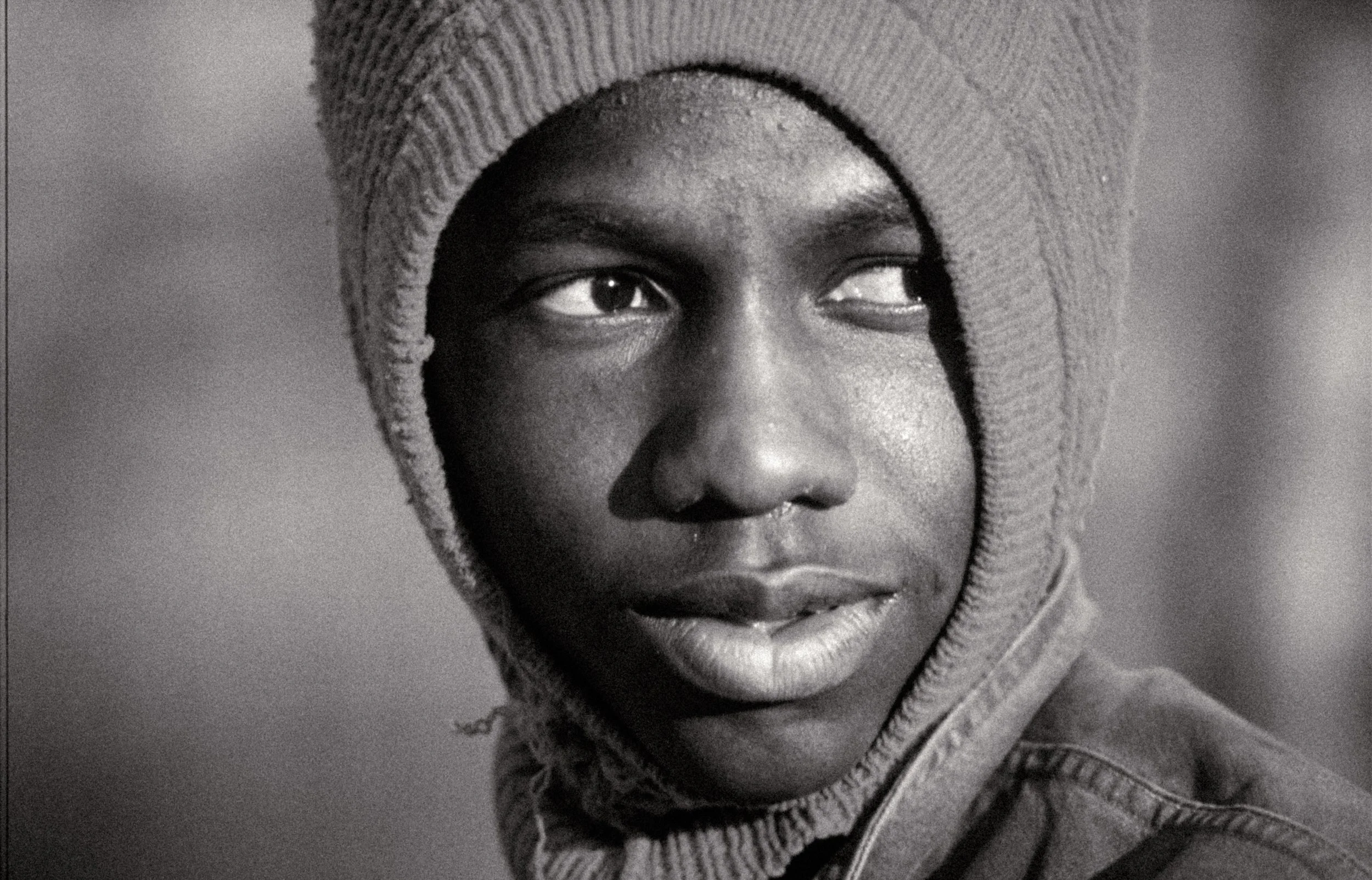 Black-and-white close-up photo of a person wearing a knit hat, with one eye looking towards the left and the other partially visible.