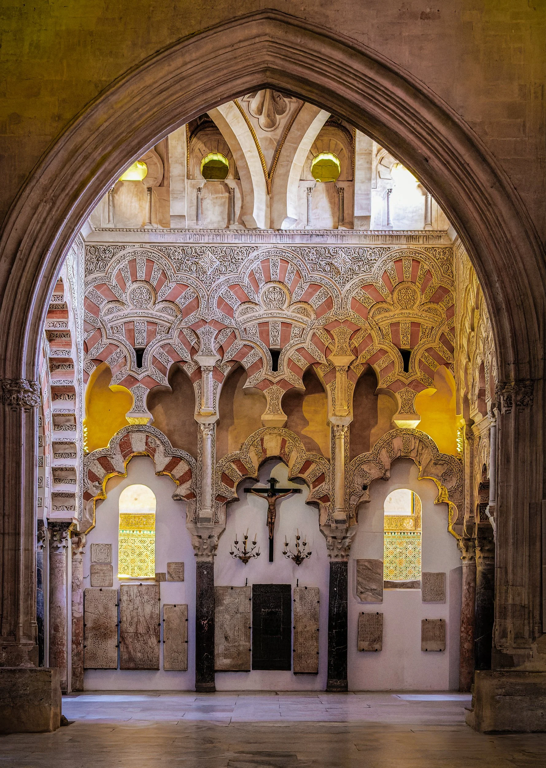 Interior of a historic church or cathedral with intricate Moroccan-style arches, a crucifix on the wall, and stained glass windows.
