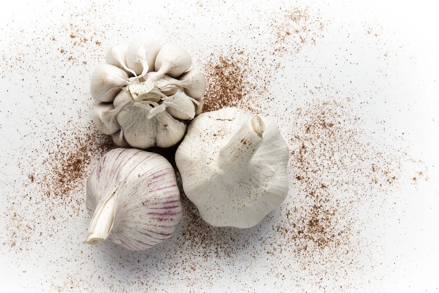 Cloves of garlic and a bulb of garlic on a white surface, sprinkled with ground spices.
