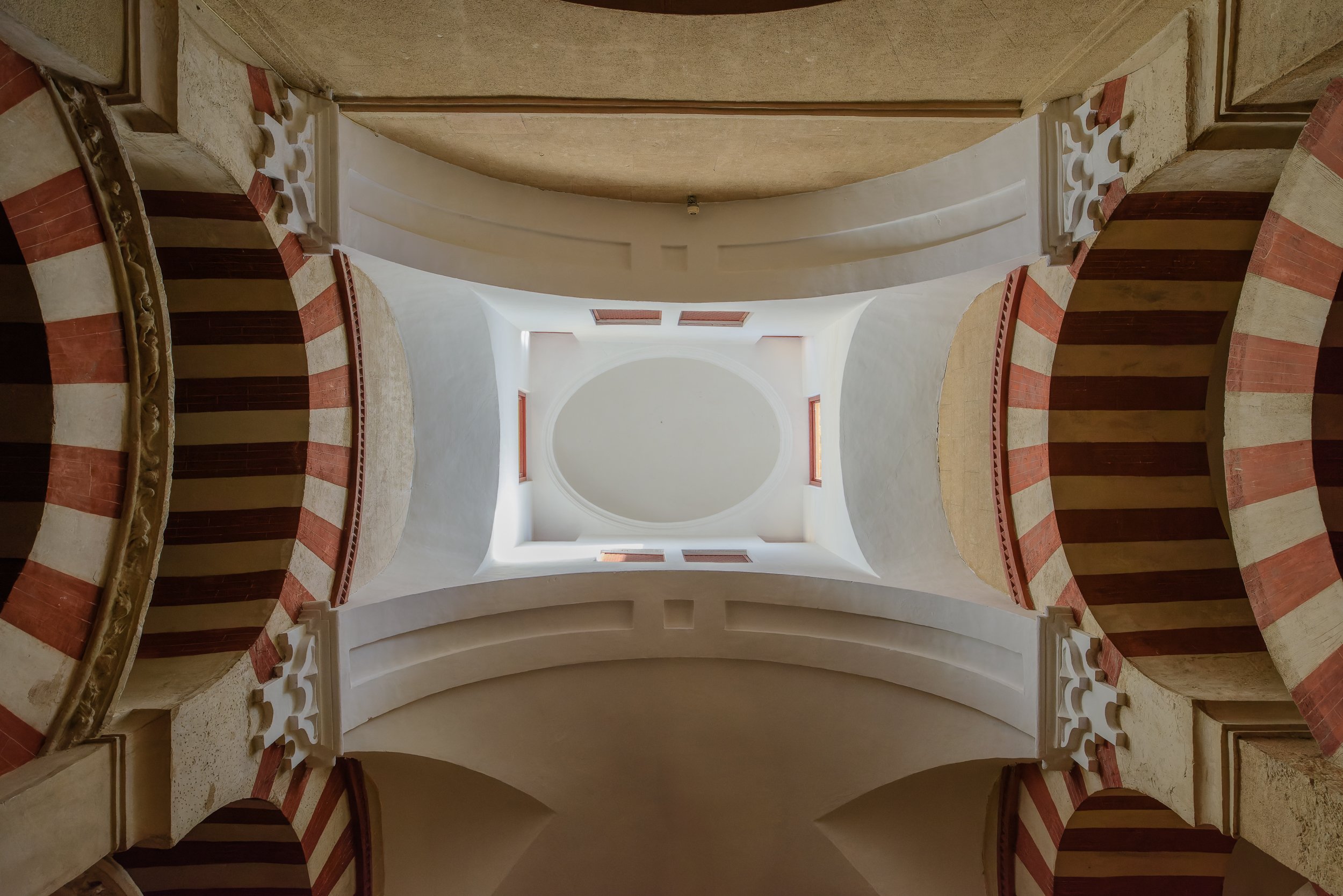 View of a church interior ceiling with white curved arches and red and beige striped columns, looking up from the ground.