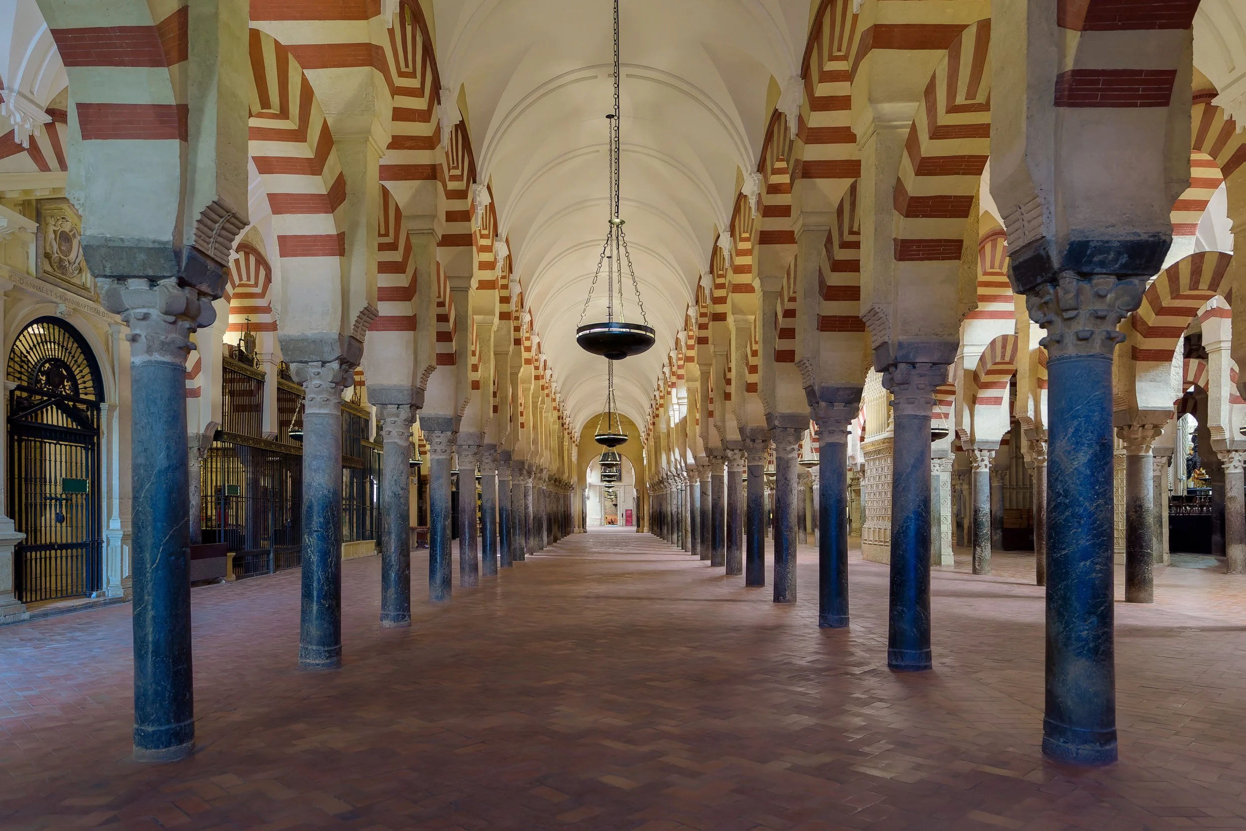 Interior view of a historical building with arches, columns, and hanging lamps.