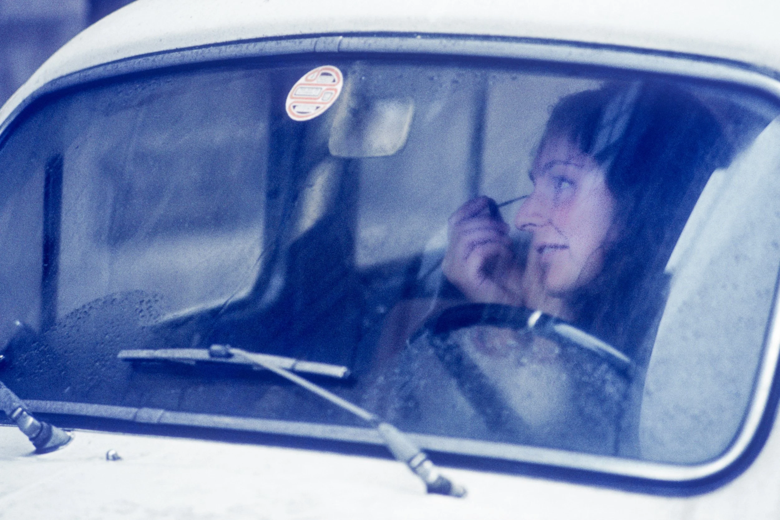 Person using a walkie-talkie inside a car, viewed through the windshield from outside.