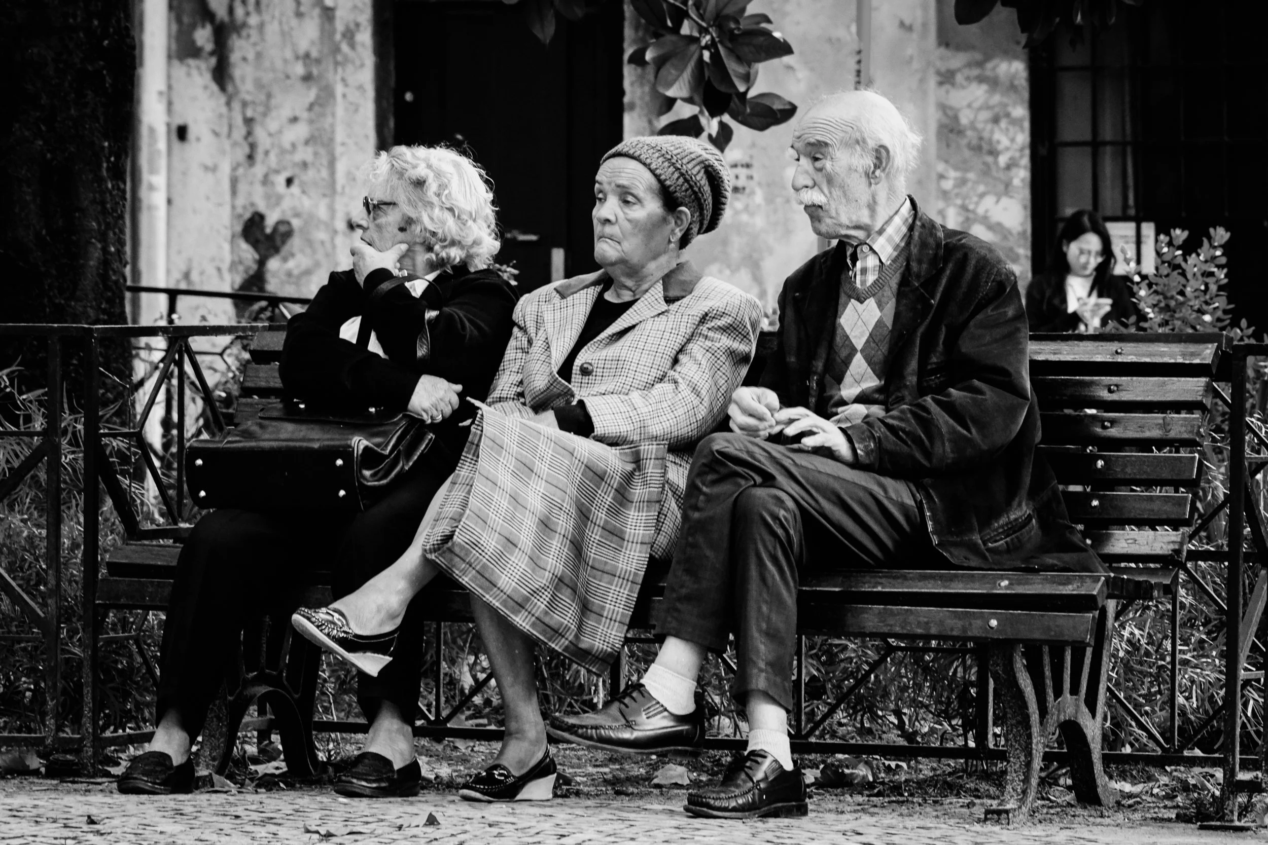 Three elderly people sitting on a bench on a small square in Lisbon, quietly observing the world around them.