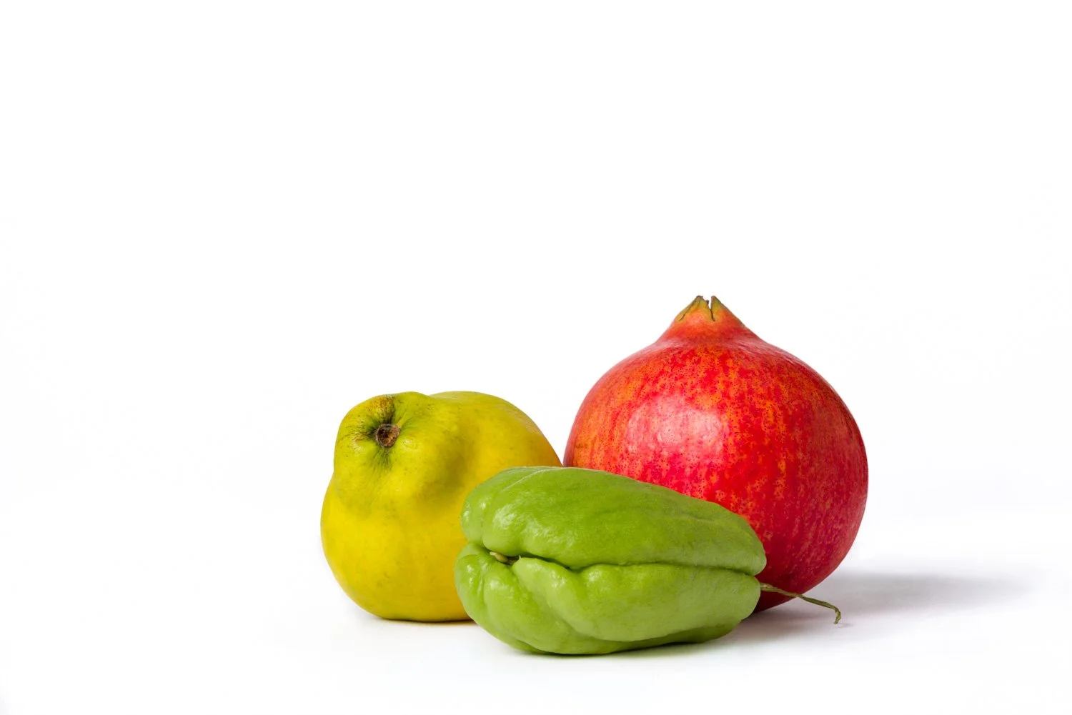Three pieces of fruit: a green apple, a pomegranate, and a chayote squash, placed on a white background.