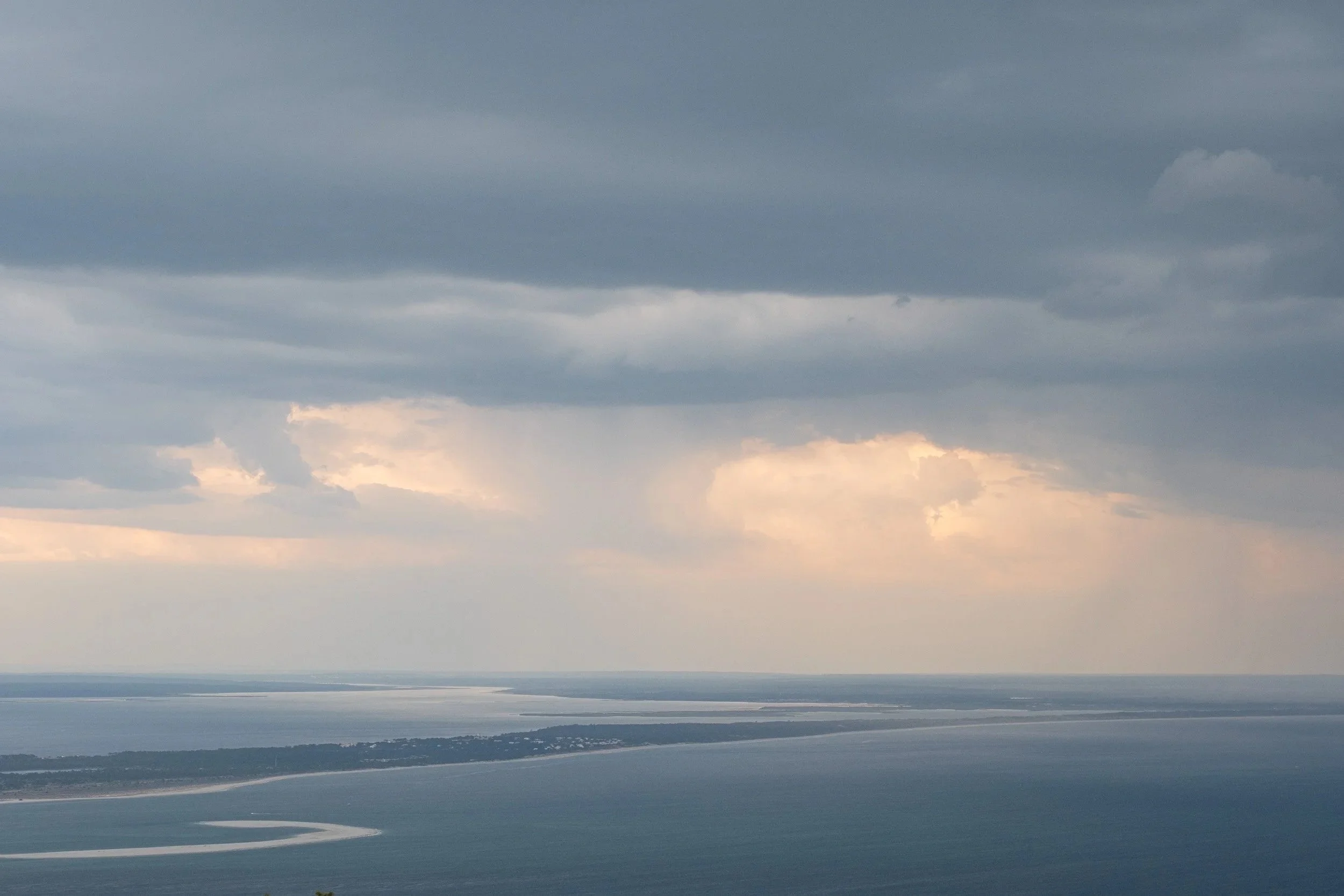Overcast sky with dark clouds over a large body of water and distant landmass with a pier or shoreline.