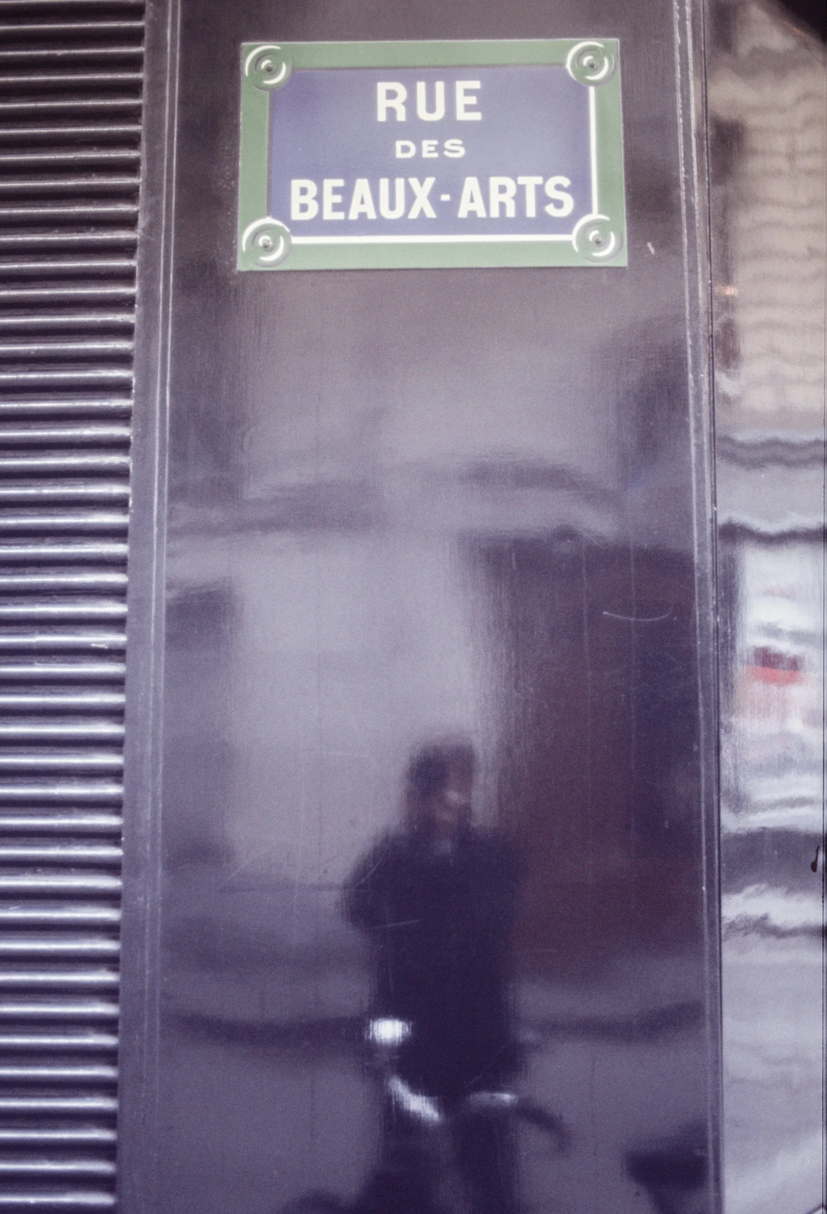Street sign reading 'Rue des Beaux-Arts' on a black wall, with a reflection of a person taking the photo.