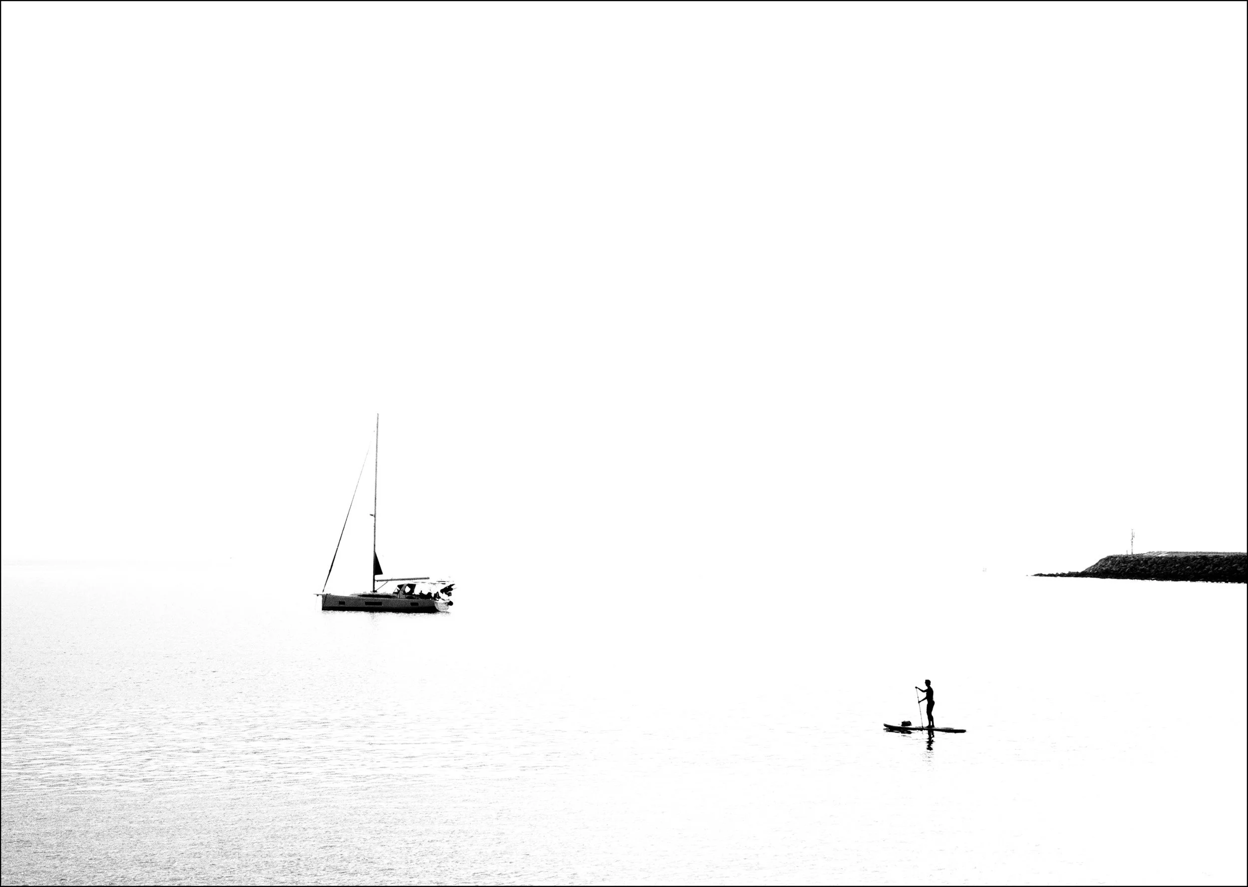 A broad bank of sea fog along the horizon delayed the sunrise, bathing the bay of L'Escala (Catalunya) in soft, diffused light. The calm sea, the anchored yacht and the solitary paddleboarder briefly came together in a scene defined by silence, simpl