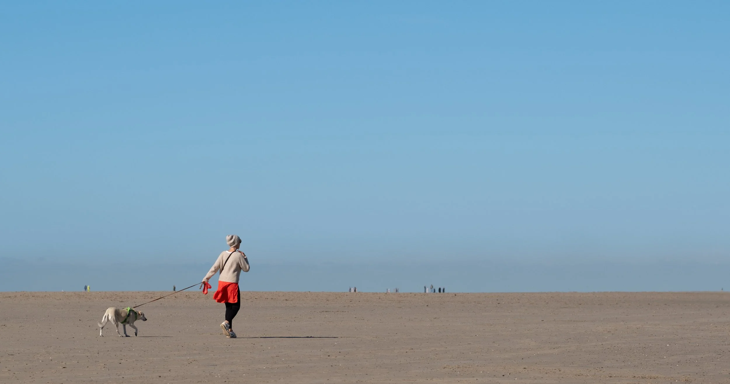 Early morning walker with her dog on a wide, peaceful beach of Schouwen-Duiveland in southwest Netherlands. The scene evokes quiet coastal beauty, empty shoreline, and a tranquil atmosphere typical of the region’s off-season serenity. 
Fujifilm X-H2 