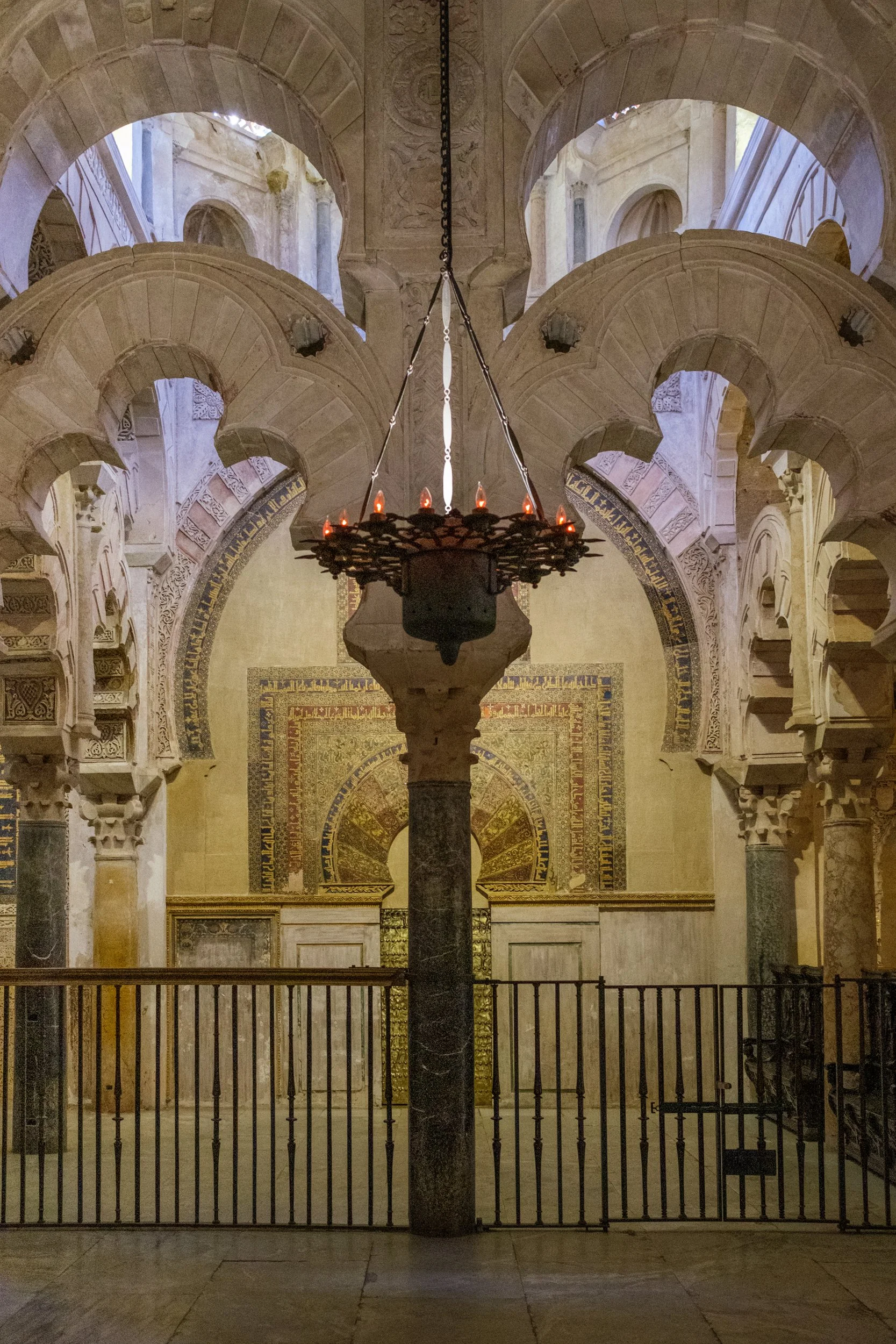 Interior of a historic building with Islamic architectural features, including arches, a chandelier with small candles, and detailed wall decorations.