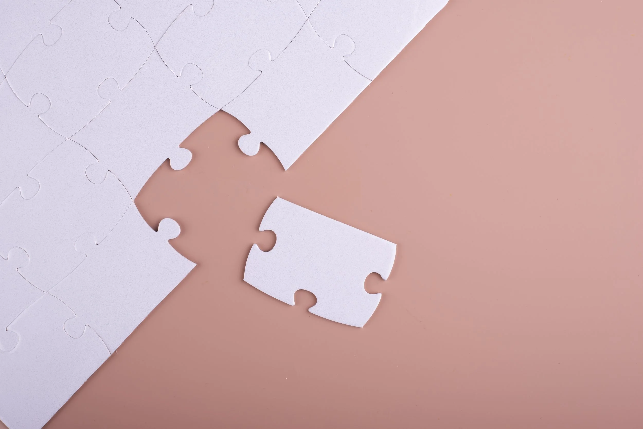 Close-up of a partially assembled white jigsaw puzzle on a pink background, with a few puzzle pieces missing.