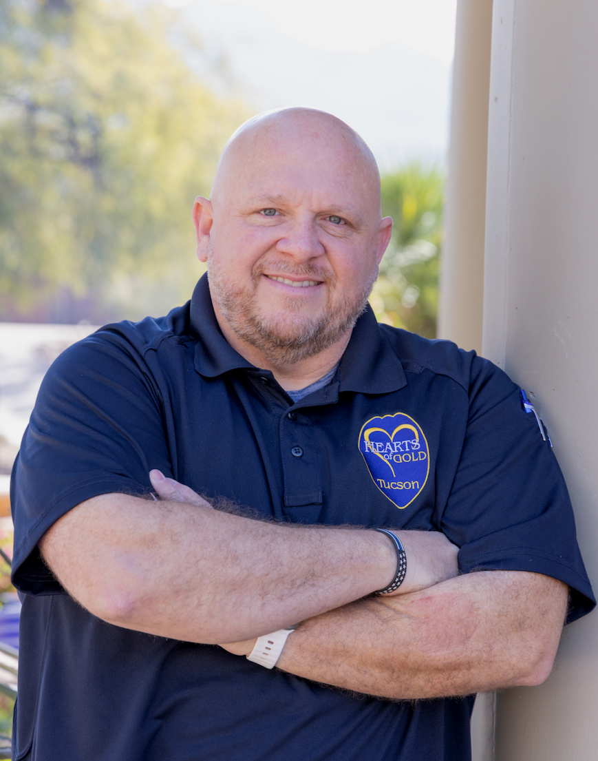 A man in a white dress shirt and red patterned tie standing outdoors in front of a fountain with a historic brick building in the background.