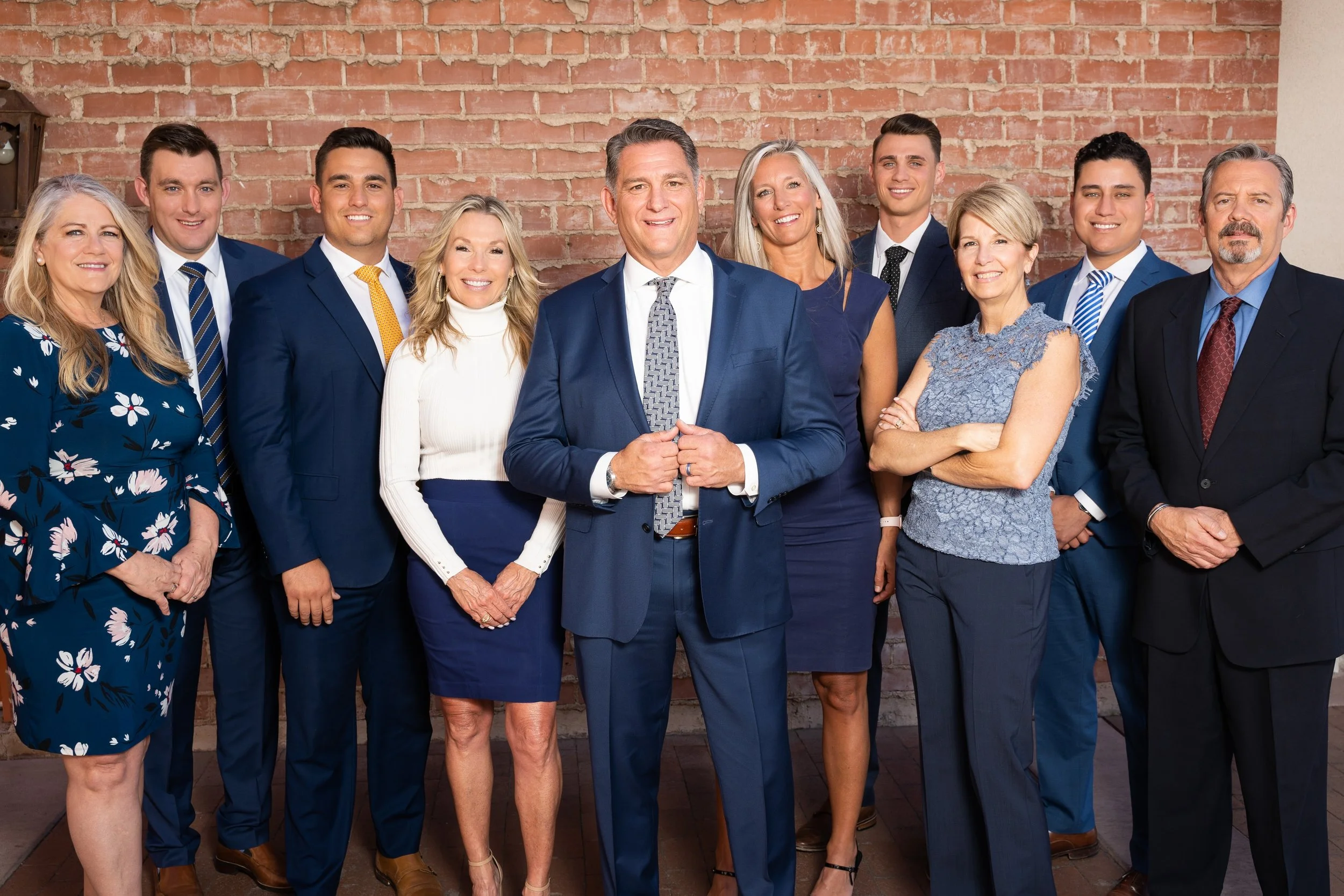 Group of ten professionally dressed people standing in front of a brick wall, smiling at the camera.