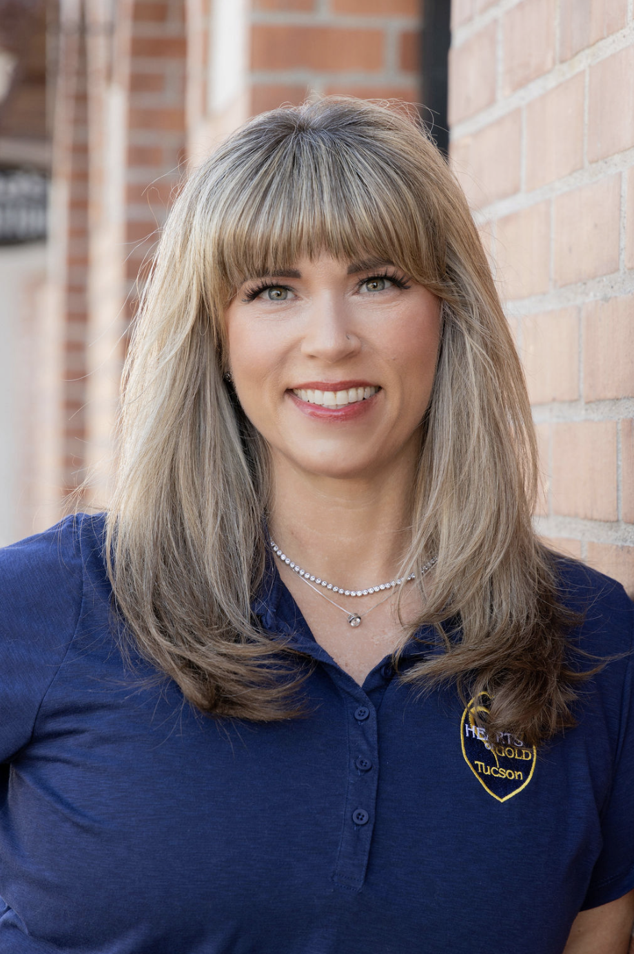 Close-up of a woman with blonde hair and blue eyes smiling, wearing a silver necklace with a pendant.