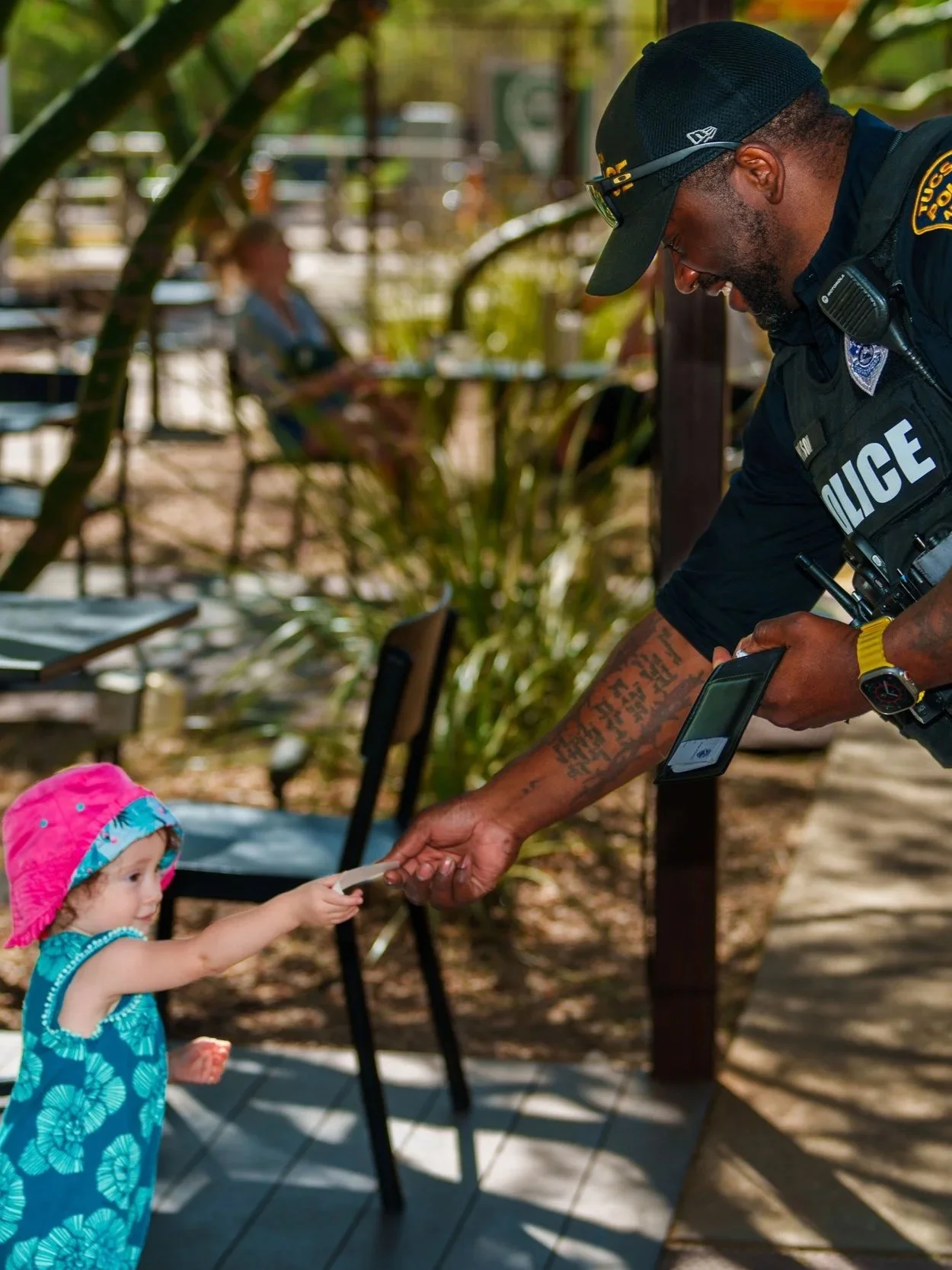 A young girl receives a card from a police officer in an outdoor setting.