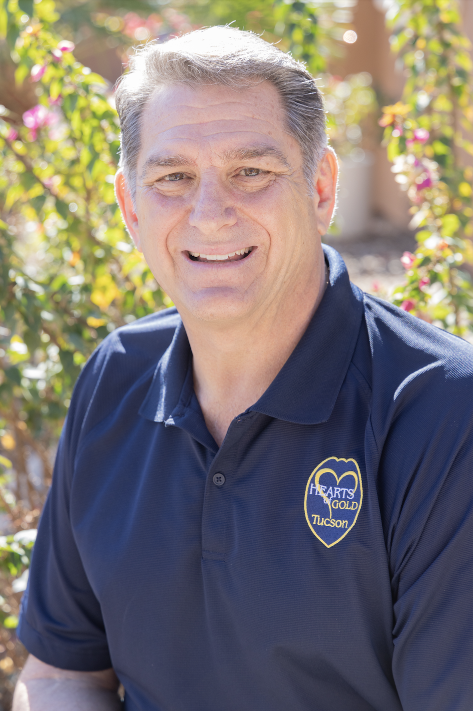 Portrait of a man in a blue jacket and white shirt, smiling, standing outdoors in front of a brick building.