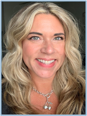 Close-up of a woman with blonde hair and blue eyes smiling, wearing a silver necklace with a pendant.