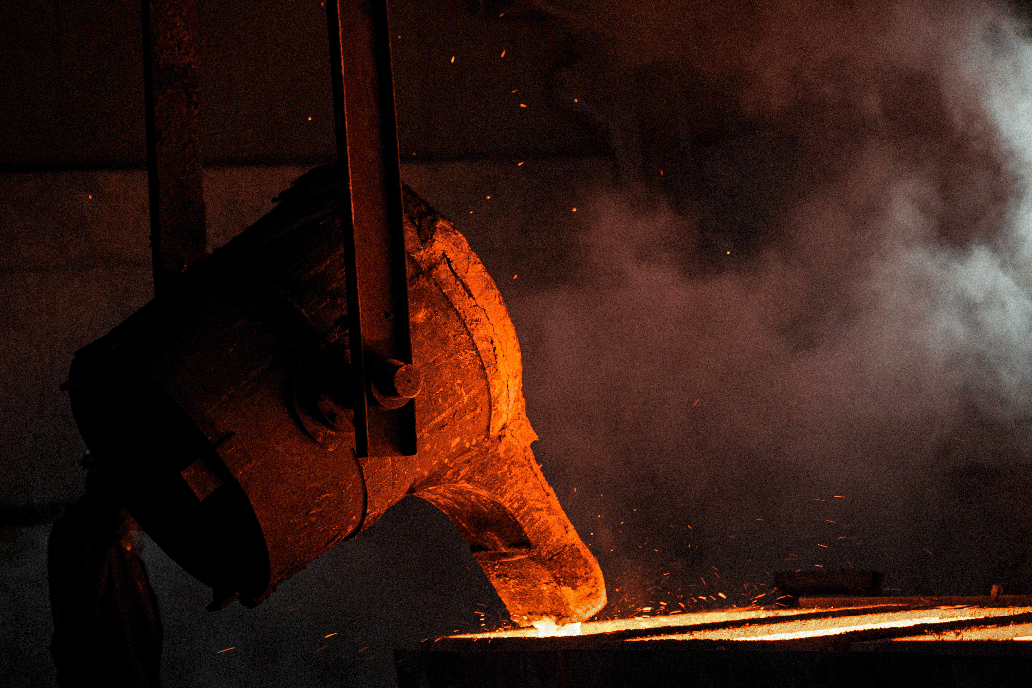 Large industrial ladle pouring molten metal in foundry environment.