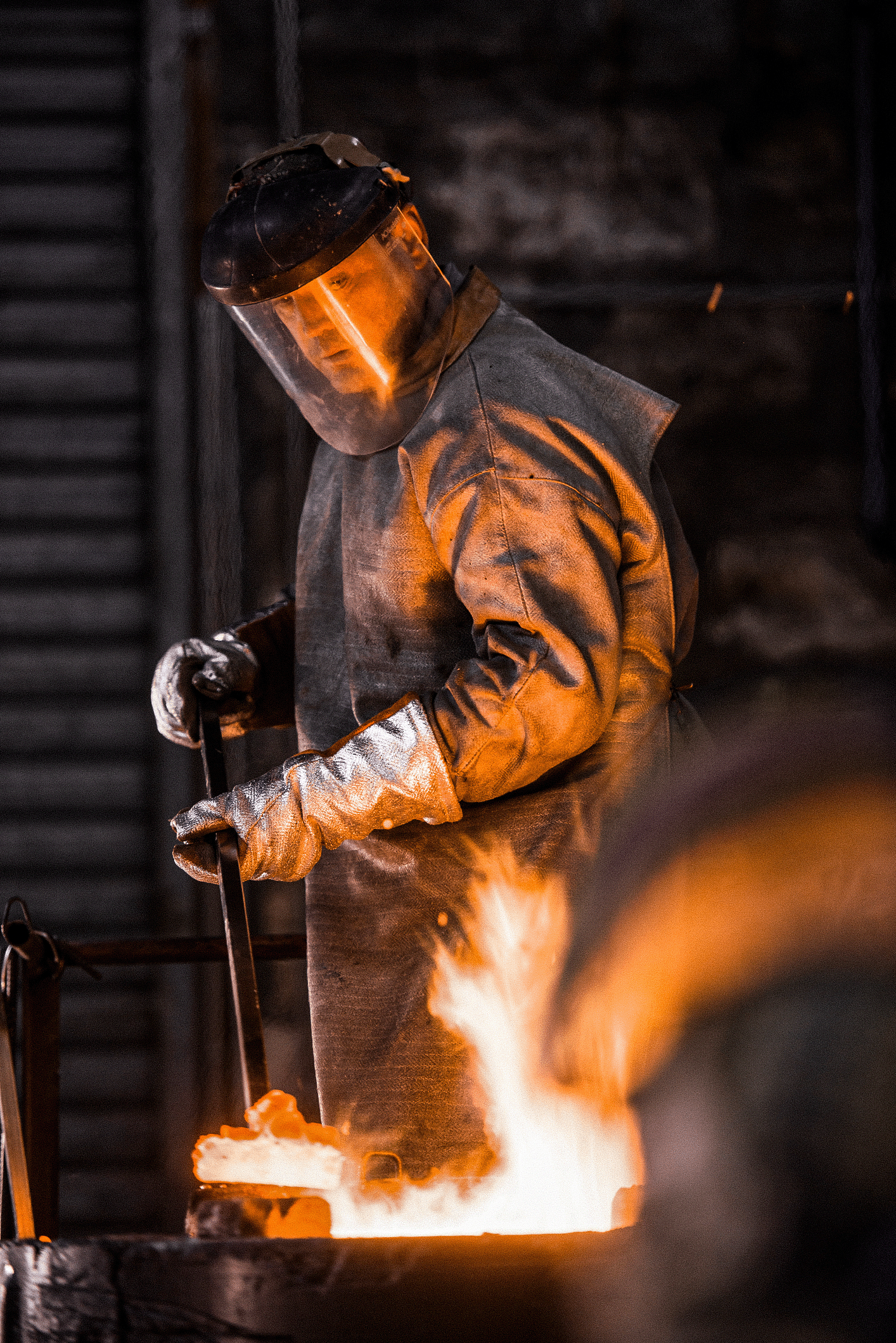 Metalworker in high-heat protective suit overseeing industrial forging process.