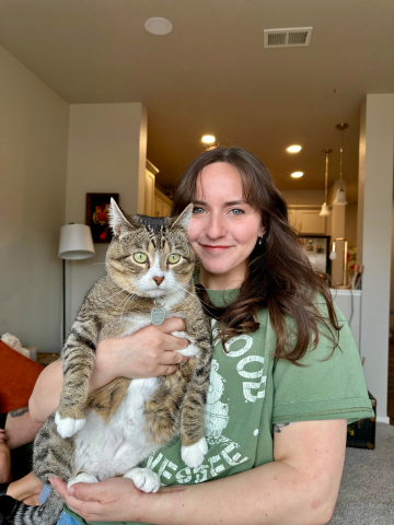 A woman with long brown hair holding a tabby cat in a living room.