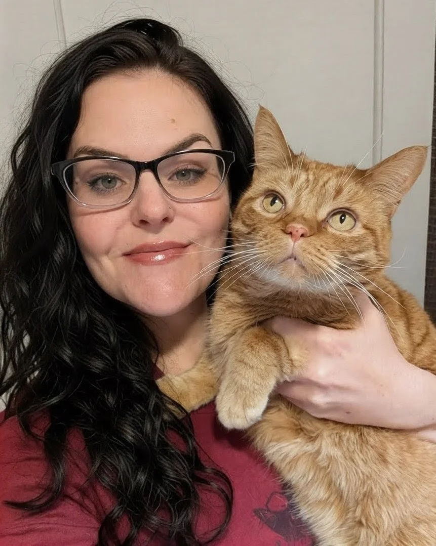 Woman with black hair and glasses holding a ginger cat.
