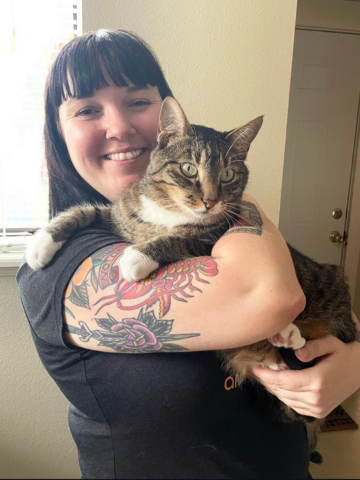 Woman with black hair smiling and holding a tabby cat inside a room