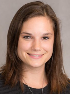 A young woman with brown hair smiling at the camera against a neutral background.