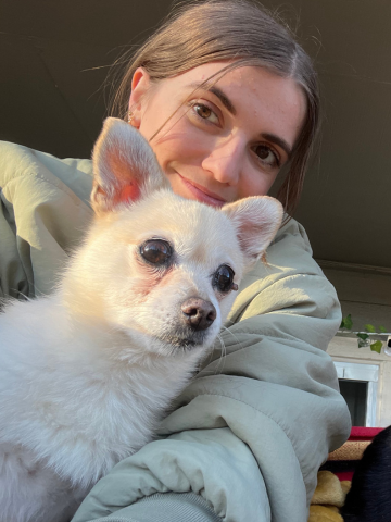 A woman smiling while cuddling a small white dog in an indoor setting.