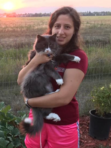 A girl holding a gray and white cat outdoors during sunset