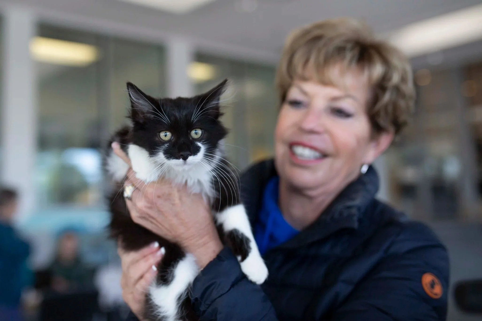 Smiling woman holding a black and white cat in an indoor setting