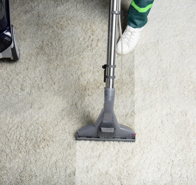 A person vacuuming a light-colored carpet with a handheld vacuum cleaner.