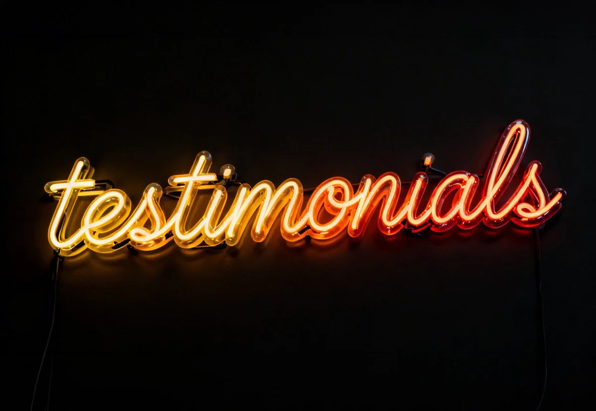 Neon sign on a black wall that reads 'testimonial's' in yellow and red lights.