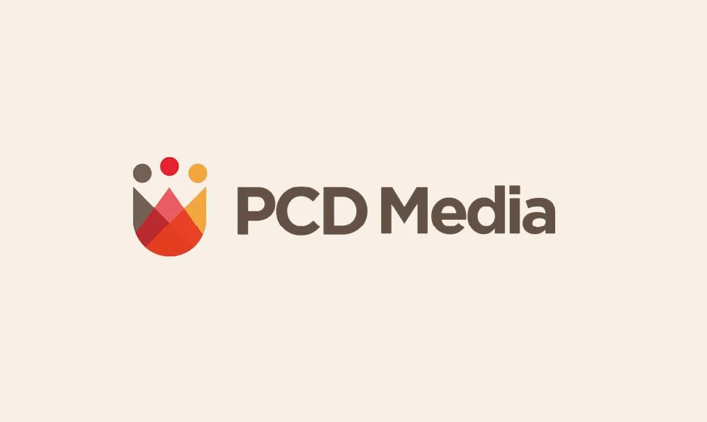 Logo of PCD Media with a stylized icon of three circles above a downward-pointing triangle, in red, orange, yellow, and black colors, on a beige background.
