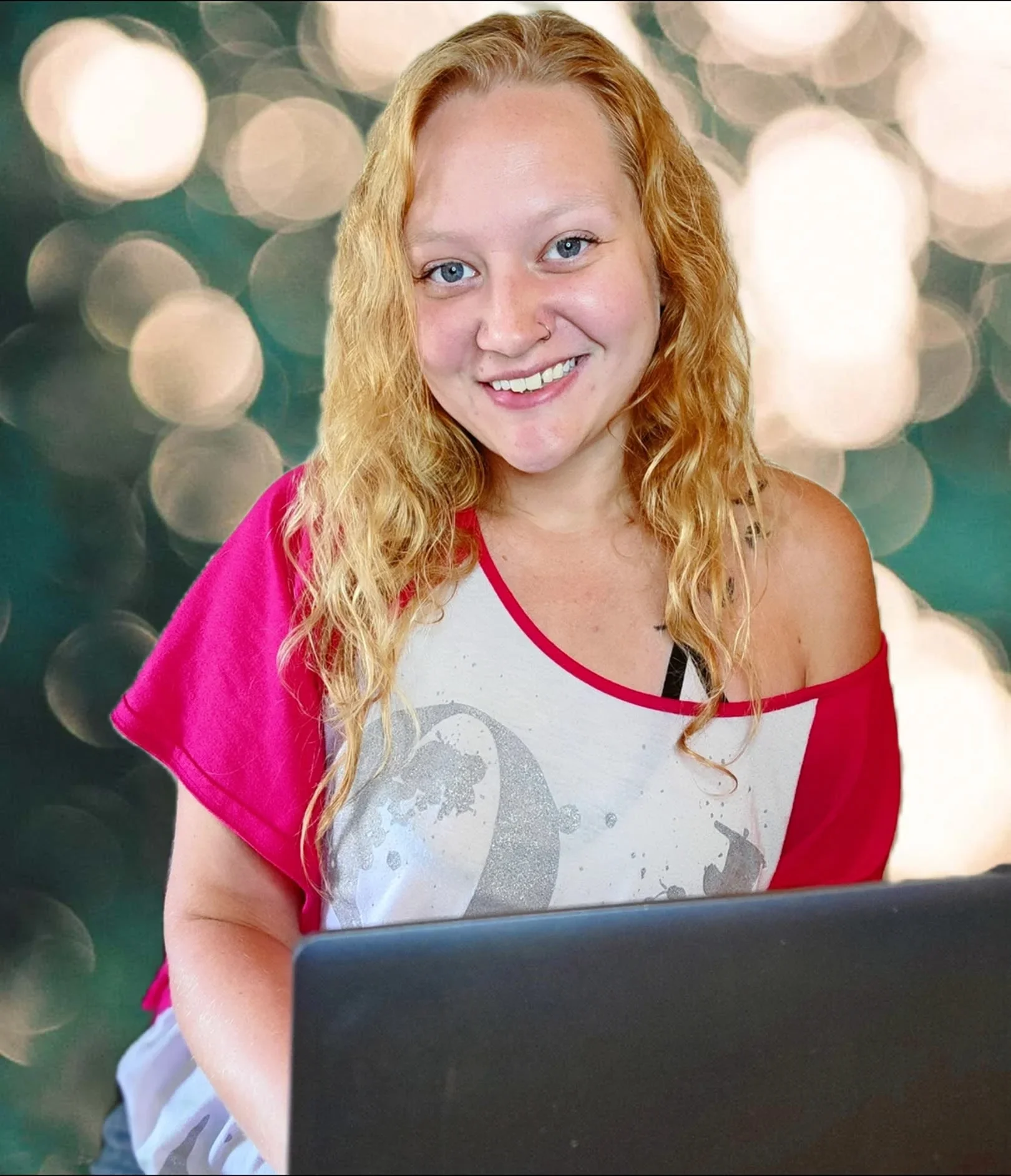 A young woman with long, curly blonde hair and blue eyes smiling at the camera. She is wearing a white and red top and sitting in front of a laptop with a blurred background of bokeh lights.