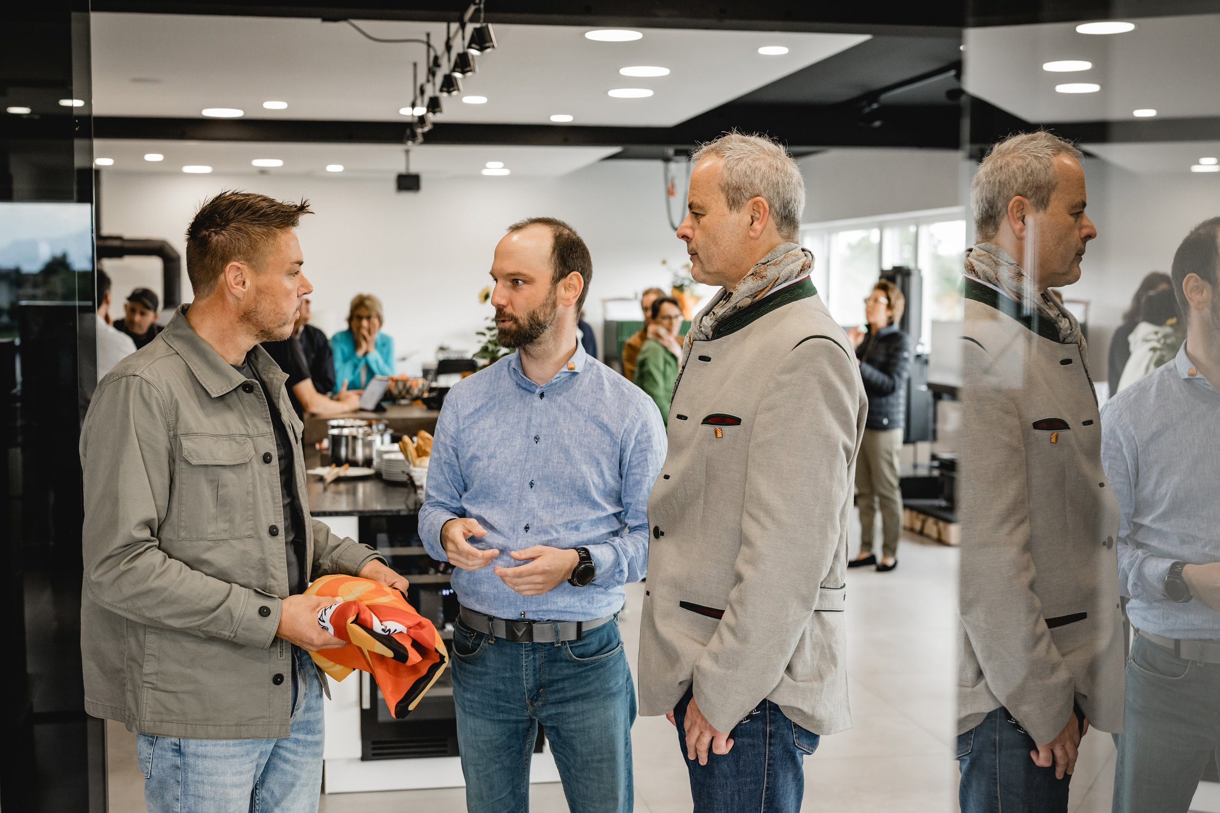 Bernhard Pupik mit zwei Männern in einem Gespräch, im Hintergrund weitere Personen in einem modernen, hellen Raum.