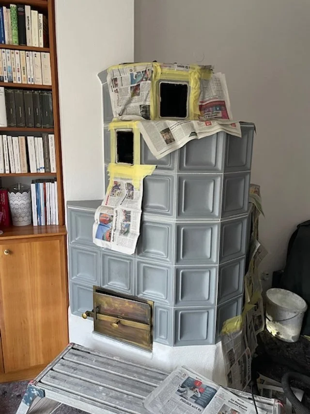 Ein Kachelofen mit blauen Kacheln, abgeklebt mit Zeitungspapier, weil er gerade von Bernhard Pupik, Ofendoktor, restauriert wird.