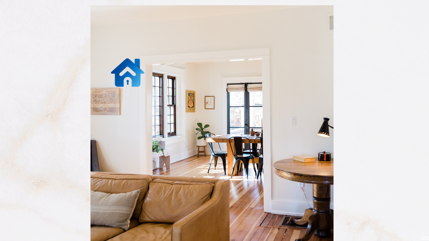 A view of a cozy living room with a tan leather sofa, a wooden side table with a lamp, and a dining area with a wooden table and black chairs, large windows, and potted plants.