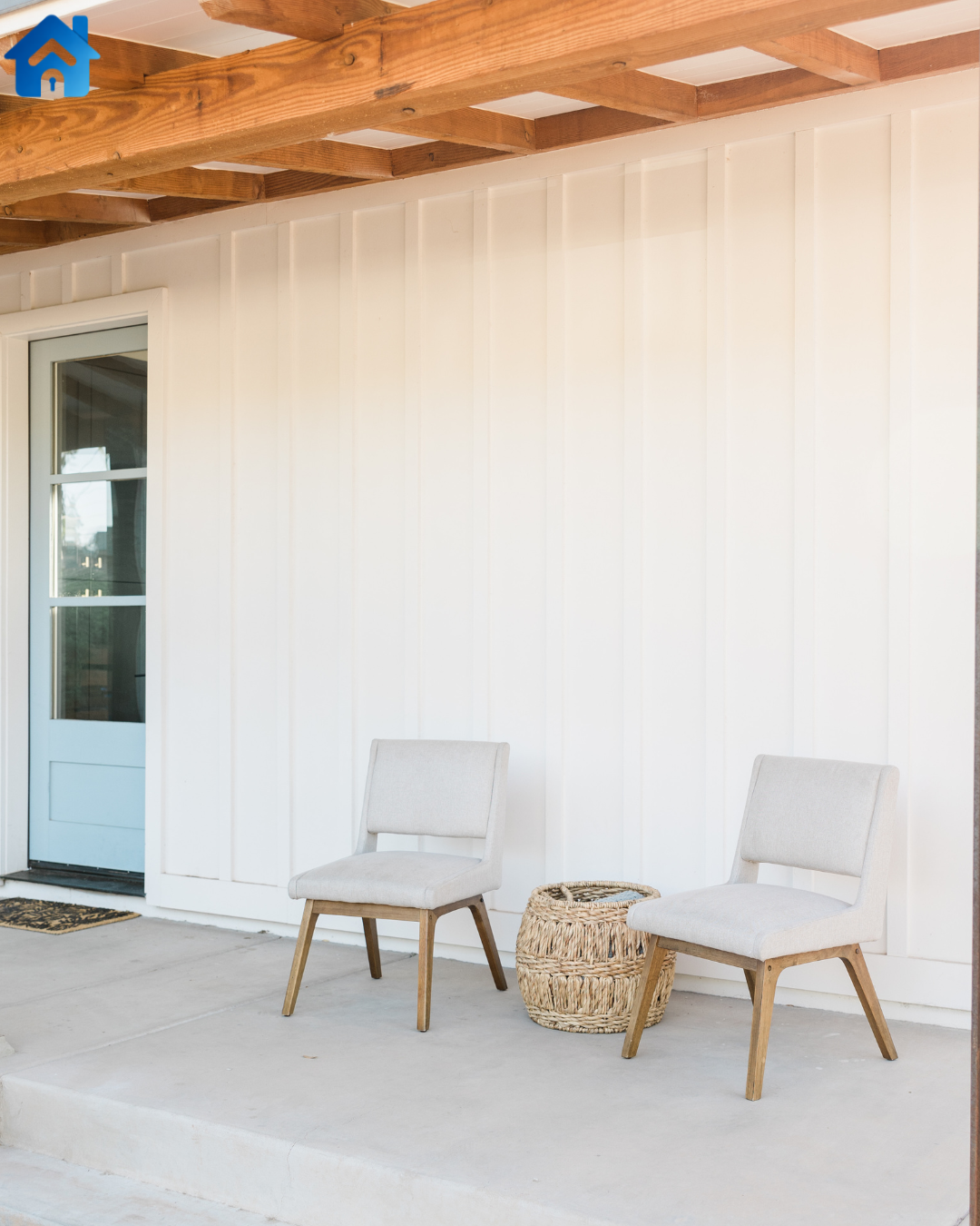 Two beige cushioned chairs and a woven basket on a porch with white siding, a door, and a wooden ceiling