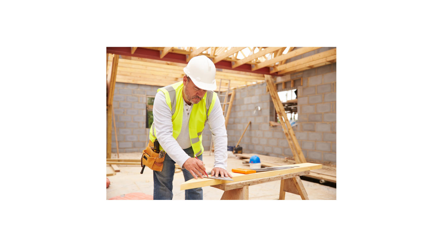 Construction worker measuring a wooden board inside a partially built structure.
